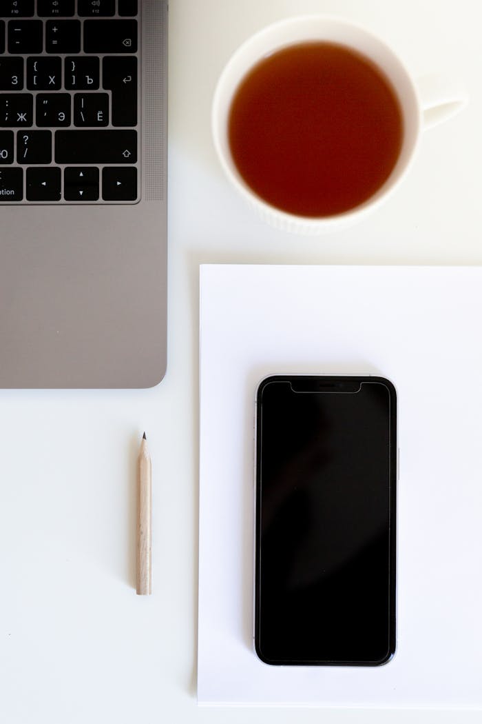 Cup of tea near laptop keyboard with smartphone on paper and wooden pencil in office